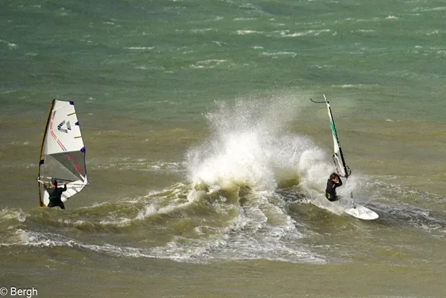 Twee windsurfers in de branding met opspattend water