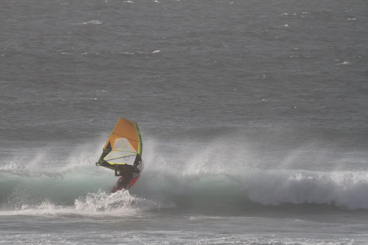 Windsurfer met geel zeil op een golf