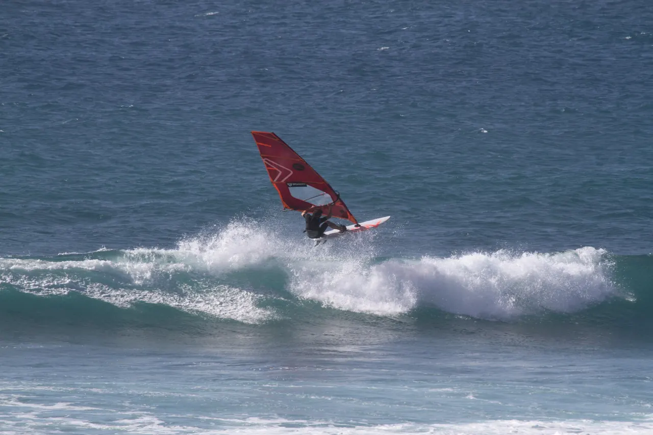Windsurfer met rood zeil boven het schuim