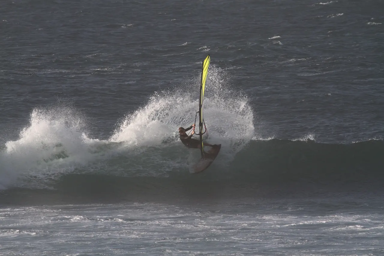 Windsurfer met geel zeil slaat spray van de lip